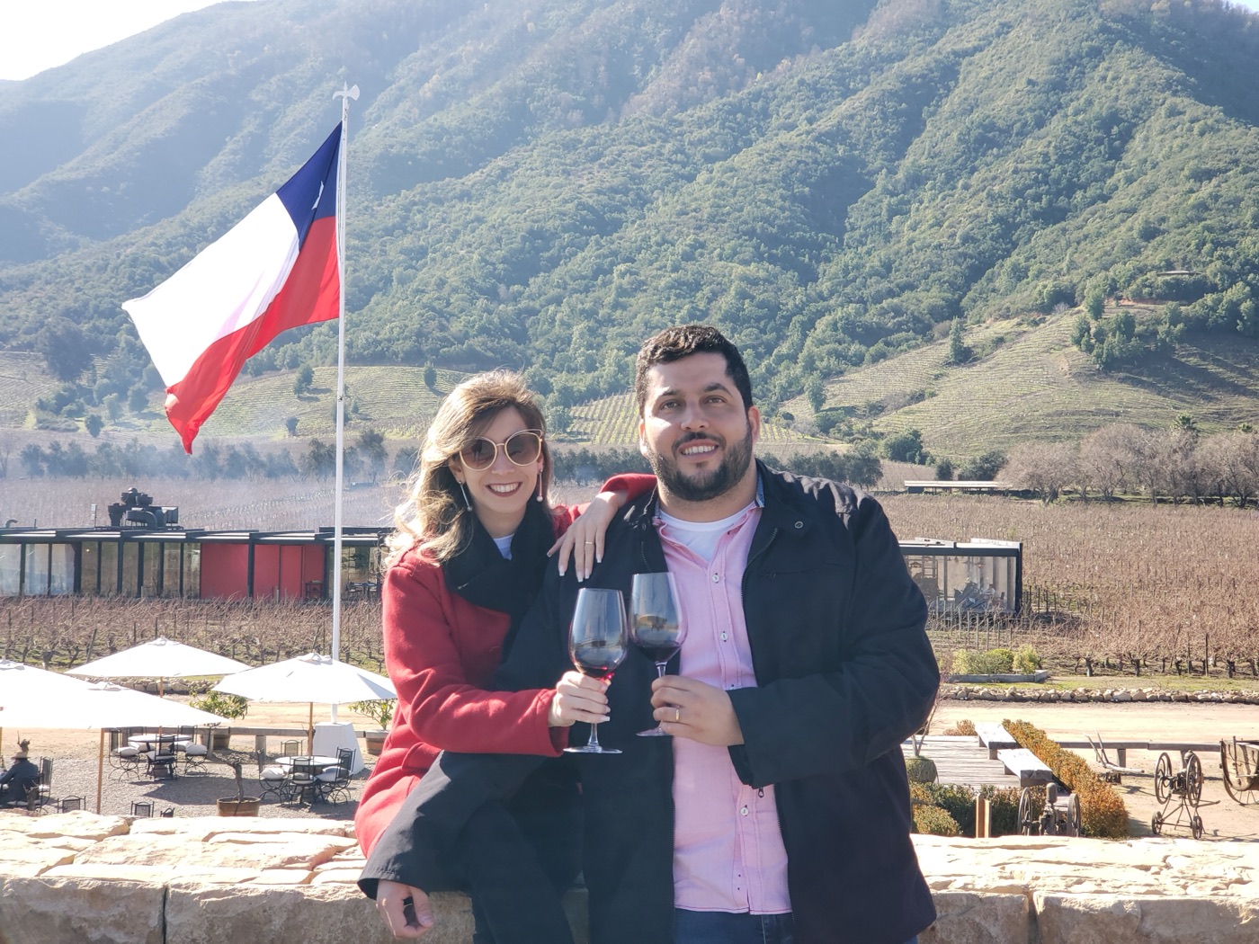 Brinde com duas taças de tinto diante dos vinhedos de Apalta, com a bandeira do Chile e a montanha ao fundo